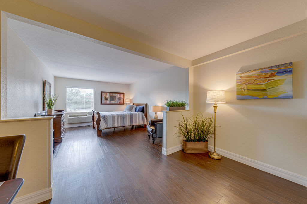 A modern open-concept living area with a cozy bedroom space, featuring wooden flooring, stylish furniture, and warm lighting.