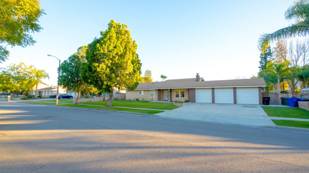 A suburban house with a large driveway and lush green lawn basking in the sunlight.
