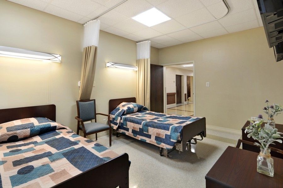 A clean and organized hospital room with two beds and chairs.