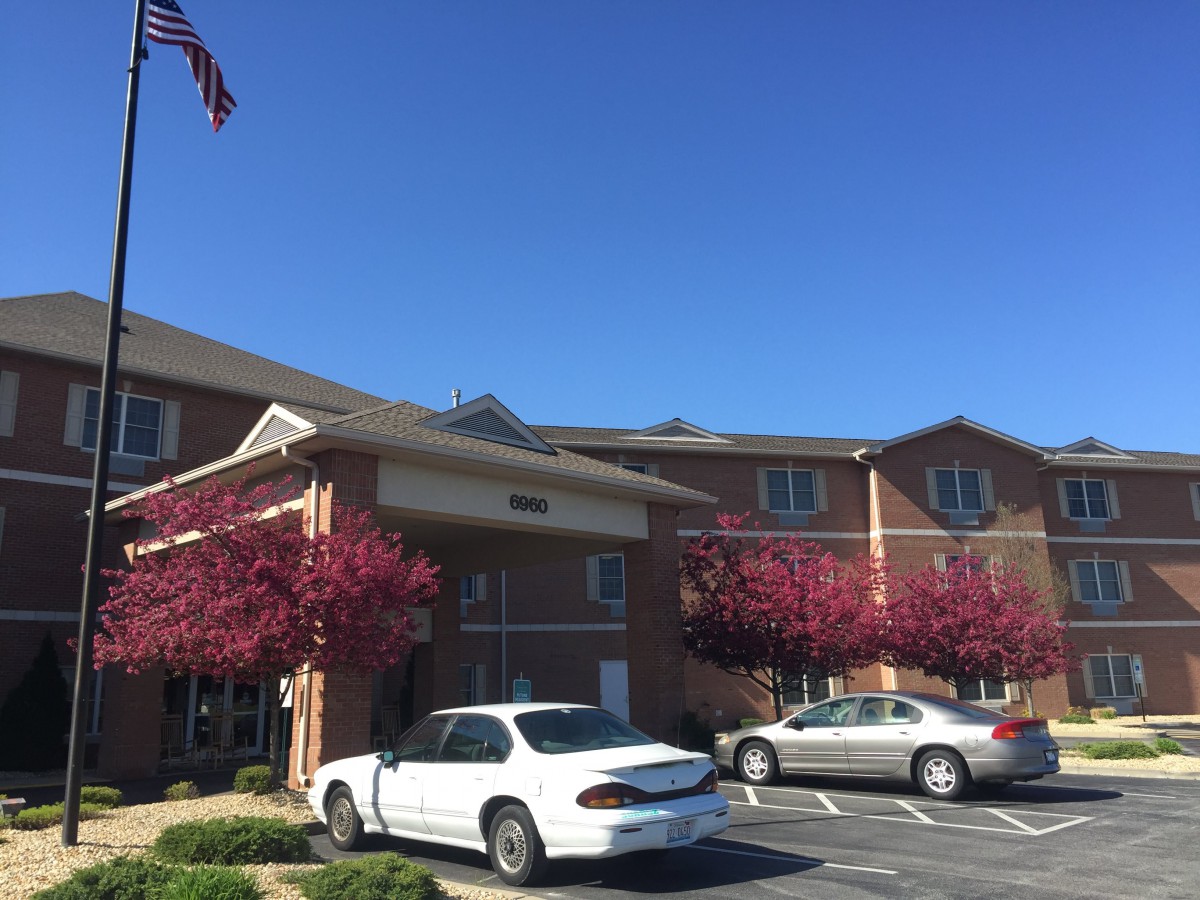 A brick building with a parking lot and two cars under a clear blue sky.