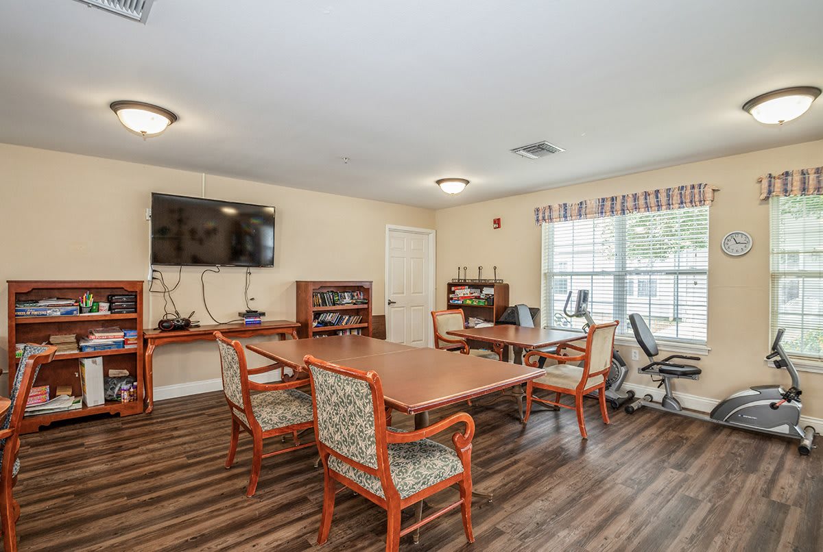 A spacious meeting room with a large conference table, chairs, and a wall-mounted television, featuring bookshelves and ample natural light from the windows.