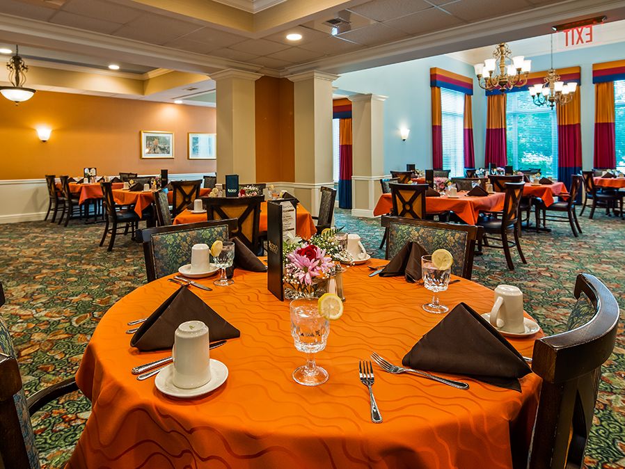 An elegantly set dining room with tables covered in orange tablecloths.