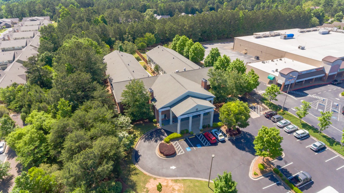 An aerial view of a large building surrounded by trees with a parking lot in the foreground.