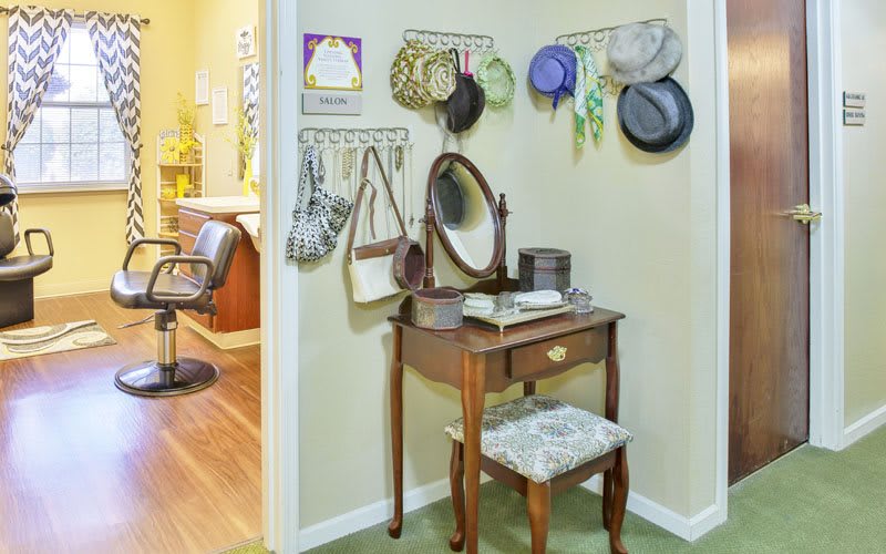 A vintage-style vanity table with a mirror, surrounded by hats and purses hanging on the wall.