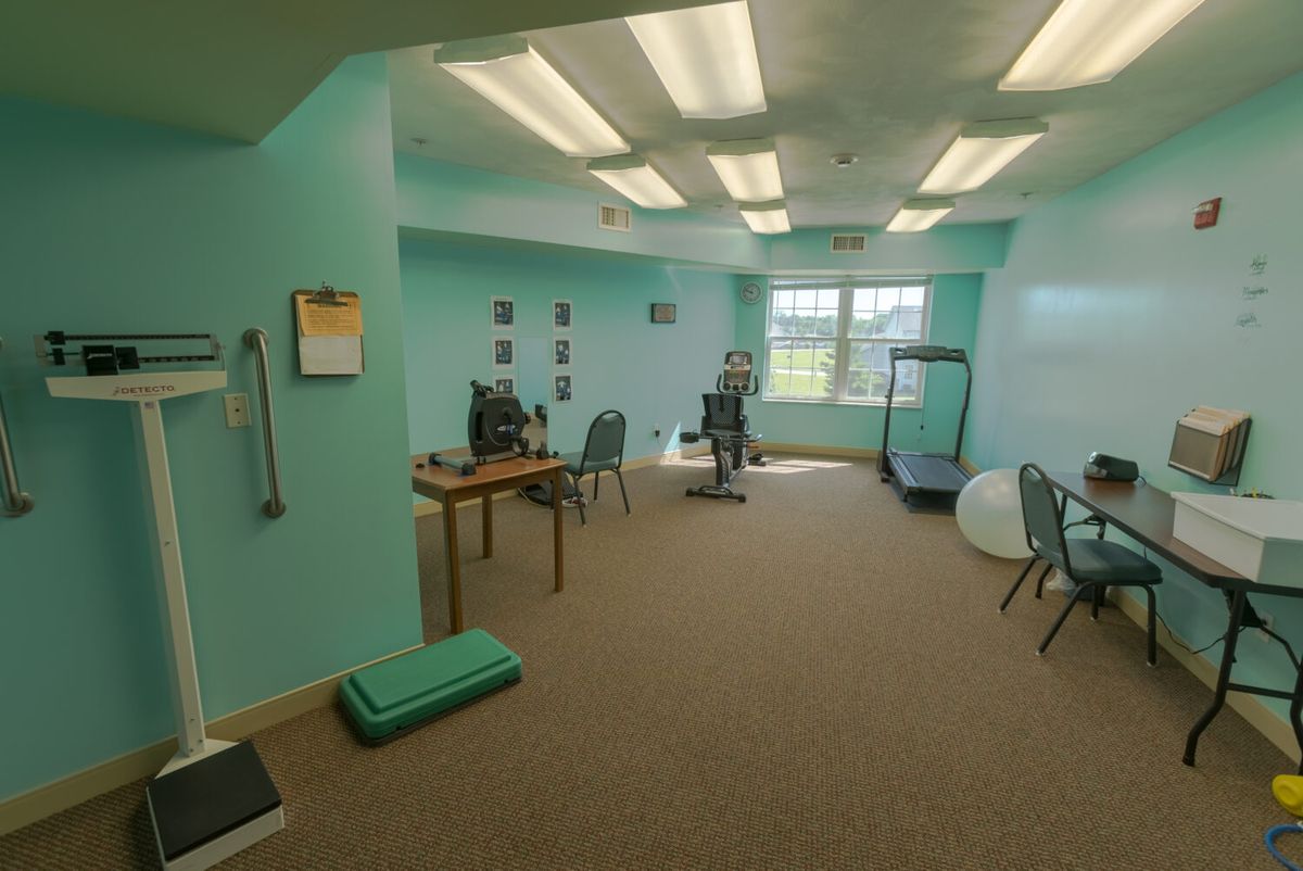A spacious office with turquoise walls featuring desks, chairs, a computer, and exercise equipment including a treadmill.