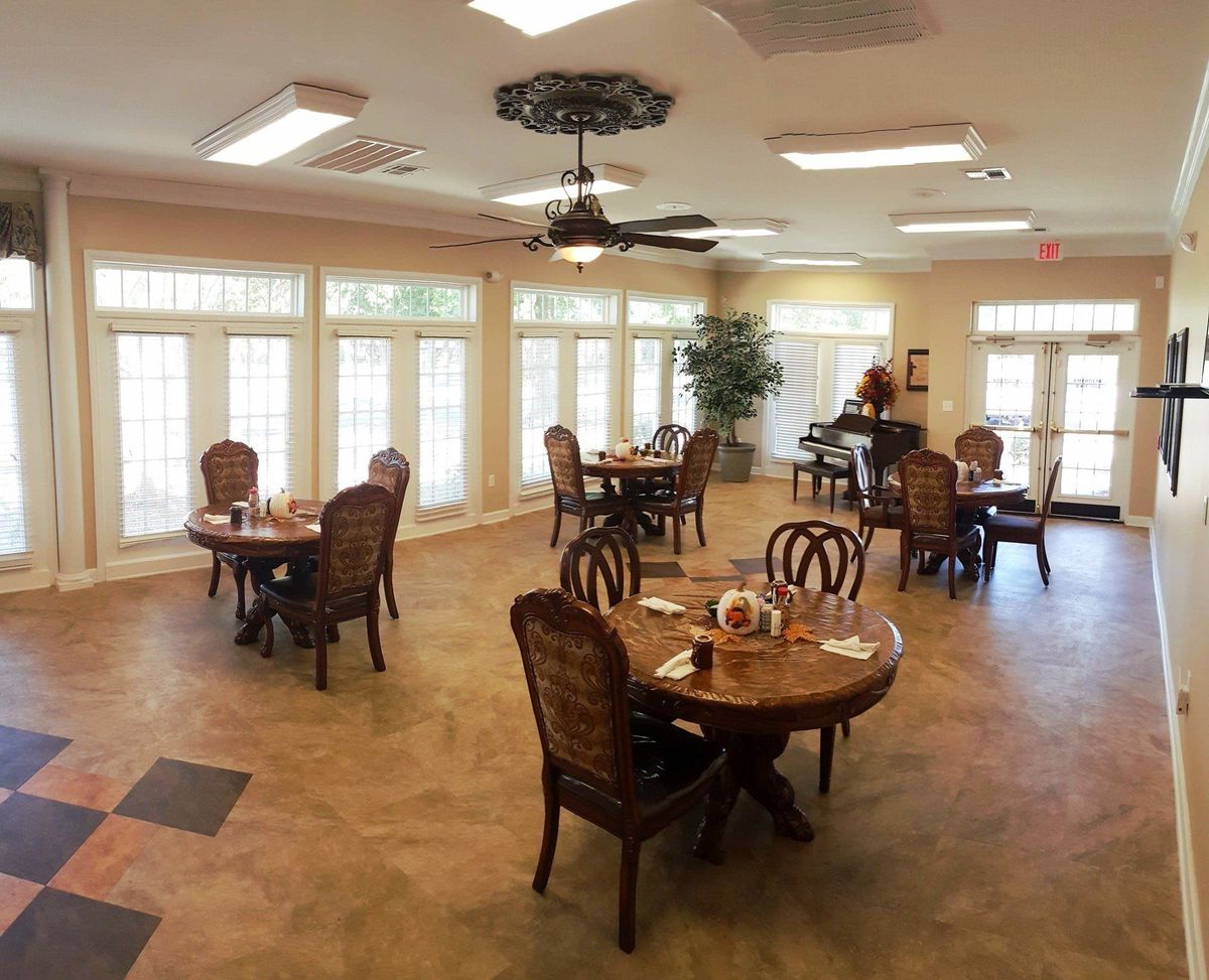 A well-lit dining room with several tables and chairs, featuring large windows and a ceiling fan.