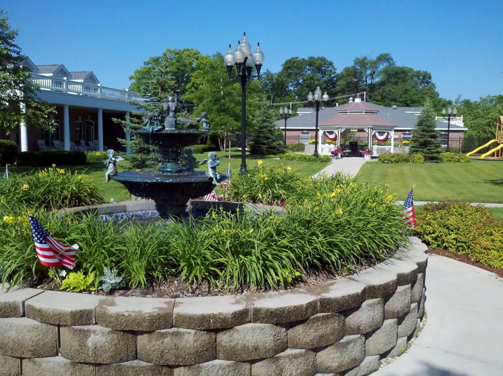 A beautiful garden with a central fountain surrounded by lush greenery and vibrant flowers, set in a well-maintained park.