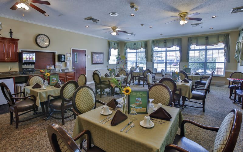 A well-arranged dining room with tables set for guests, featuring elegant decor and large windows.