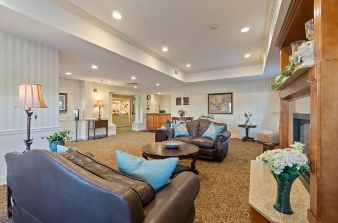 A cozy lounge area furnished with sofas, a coffee table, and decorative elements, featuring carpeted flooring and soft lighting.