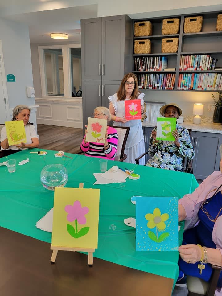 A group of individuals showcasing their colorful flower paintings during an indoor art activity.