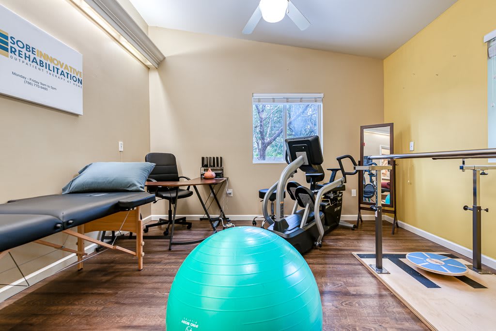 A cozy home gym setup featuring a yoga ball, stationary bike, and therapy table in a well-lit room.