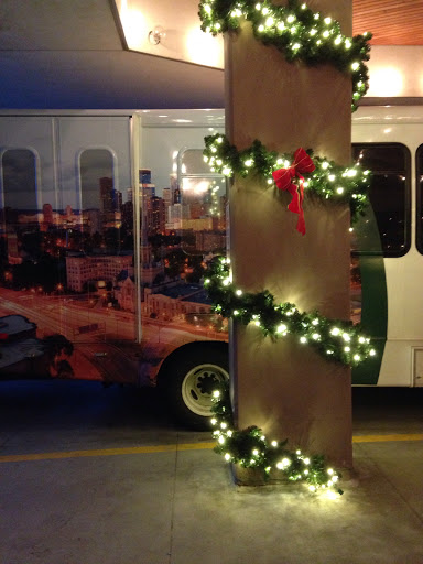 A festive display featuring Christmas garland and lights wrapped around a pillar, with a decorated bus in the background.