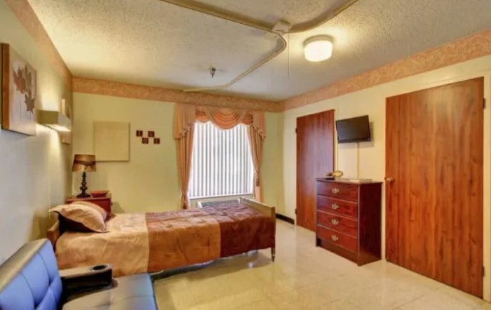 A cozy bedroom featuring a single bed, dresser, and wall-mounted TV.