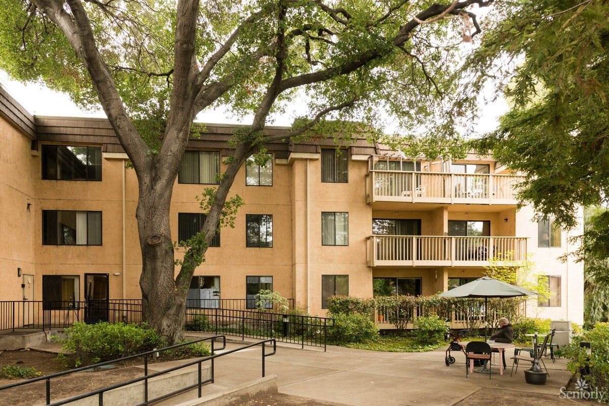 A residential apartment building with a garden and large tree in the courtyard.