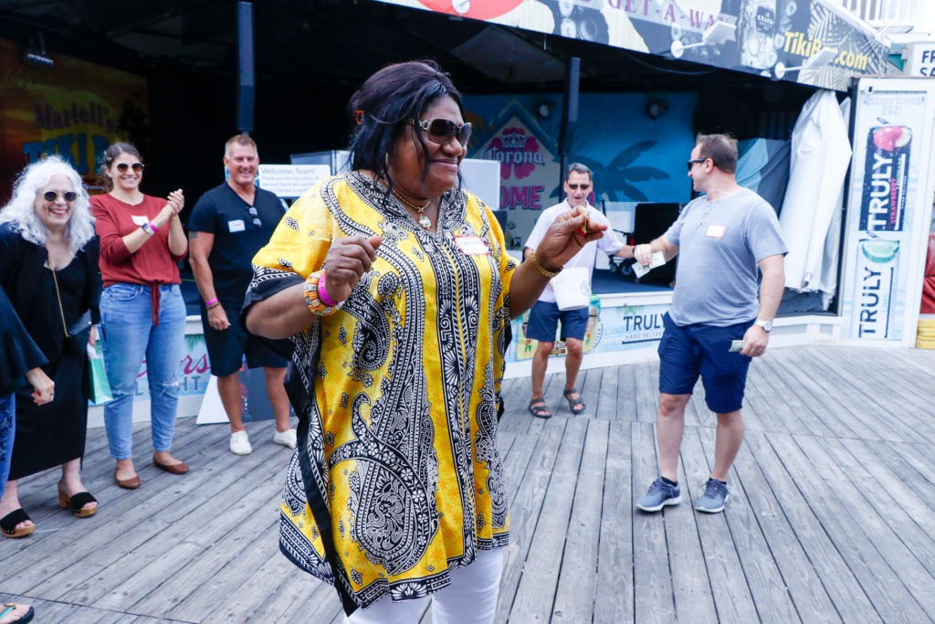 A woman in vibrant attire dances joyfully among a group of people outdoors.