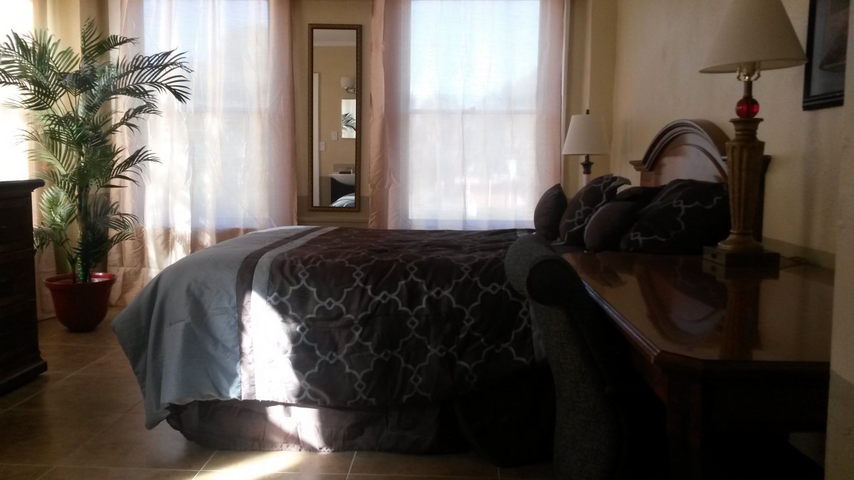 A cozy bedroom with a large bed and sunlight streaming through the windows.