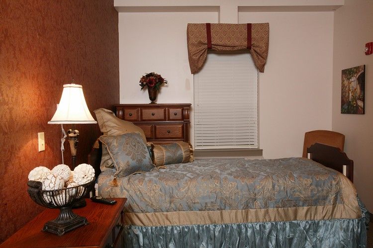 A cozy bedroom featuring a bed with decorative pillows, a nightstand with a lamp, and a window adorned with drapes.