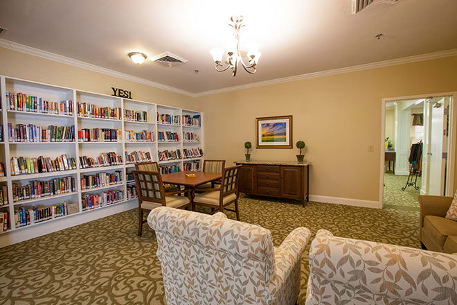 A cozy library room with bookshelves, comfortable chairs, and a table for reading.