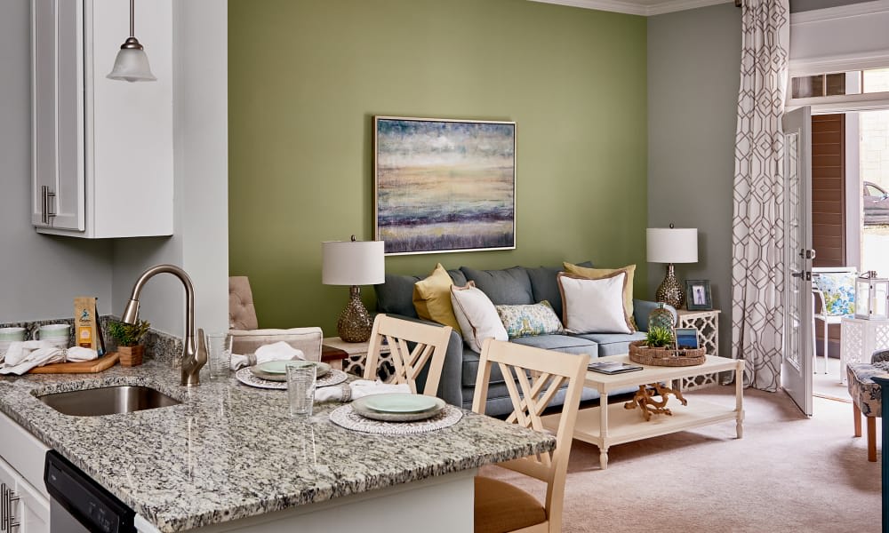 A stylish living room with a green accent wall, featuring a comfortable sofa, tasteful artwork, and a dining area adjacent to a kitchen counter.