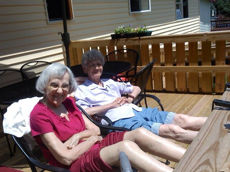 Two elderly individuals sitting and relaxing on a sunny deck.
