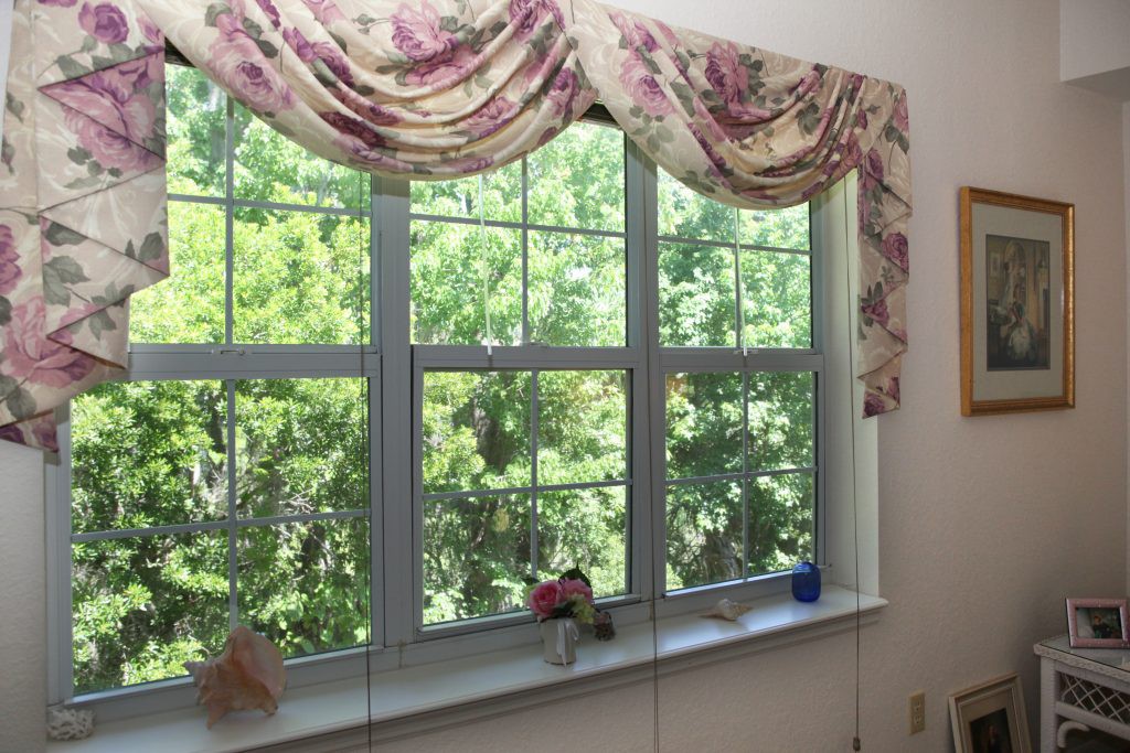 A window with floral-patterned valance, allowing natural light to brighten the interior and revealing a view of lush, green trees outside.