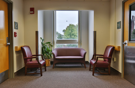 A cozy waiting area featuring a sofa, two chairs, and a plant by the window.