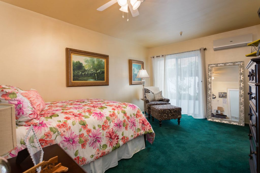 A cozy bedroom featuring a floral bedspread, green carpet, and natural lighting.