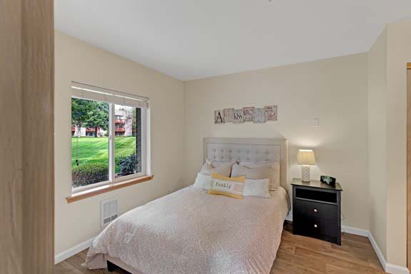 A cozy bedroom featuring a bed with a tufted headboard, a nightstand with a lamp, and a window overlooking greenery.