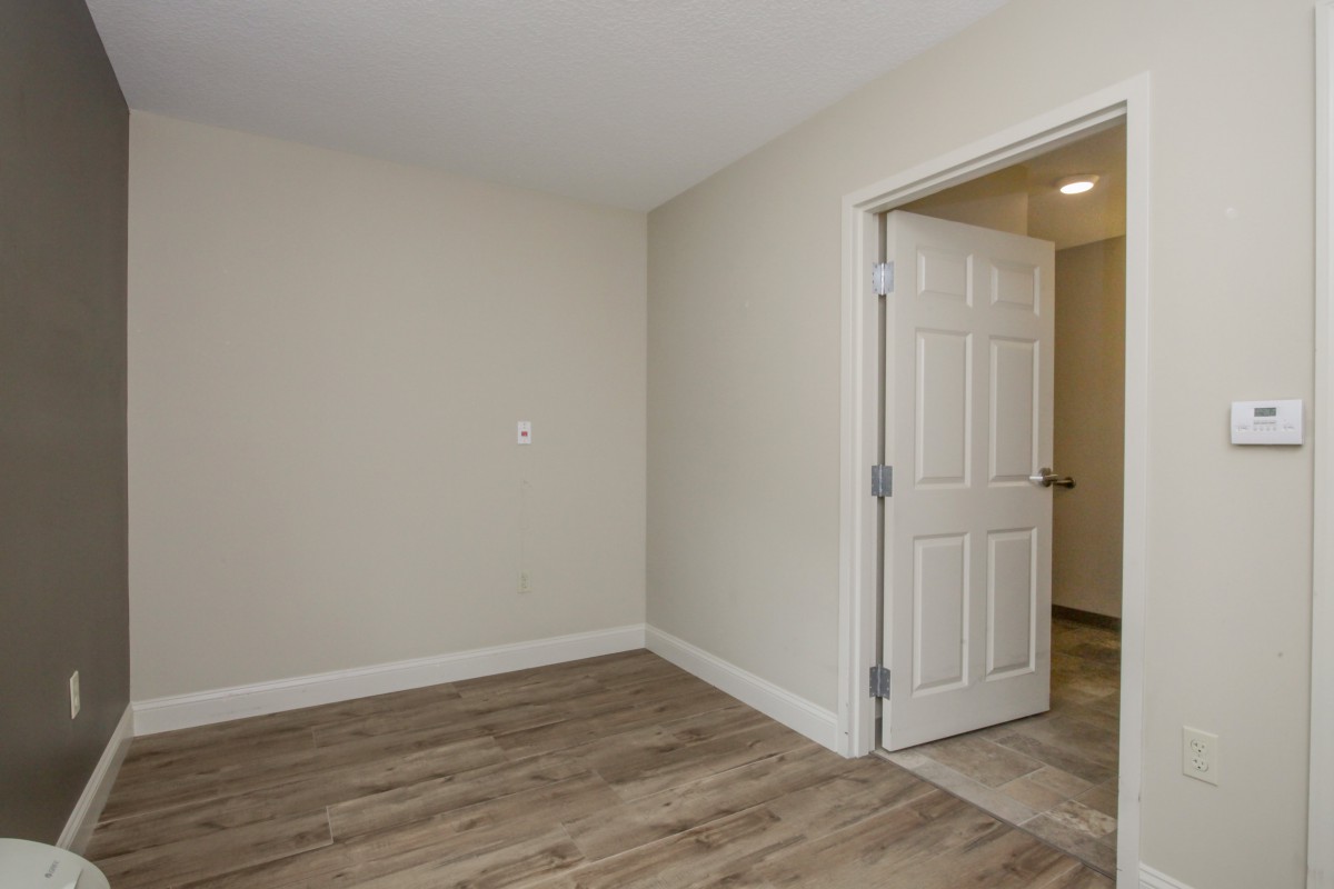 A view of an empty room with wooden flooring and a partially open door, showcasing minimalistic design.