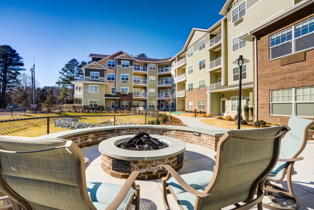 An inviting outdoor space with a fire pit and seating area in front of a modern apartment building.