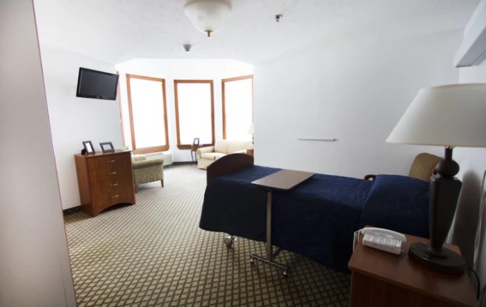 A spacious hospital room with a patient bed, television, and seating area by large windows.
