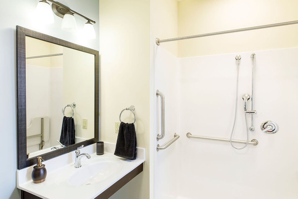 A clean and modern bathroom featuring a sink with a mirror, towel, and a walk-in shower.
