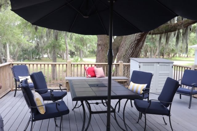 A cozy patio setup with chairs and a table under an umbrella on a wooden deck surrounded by nature.