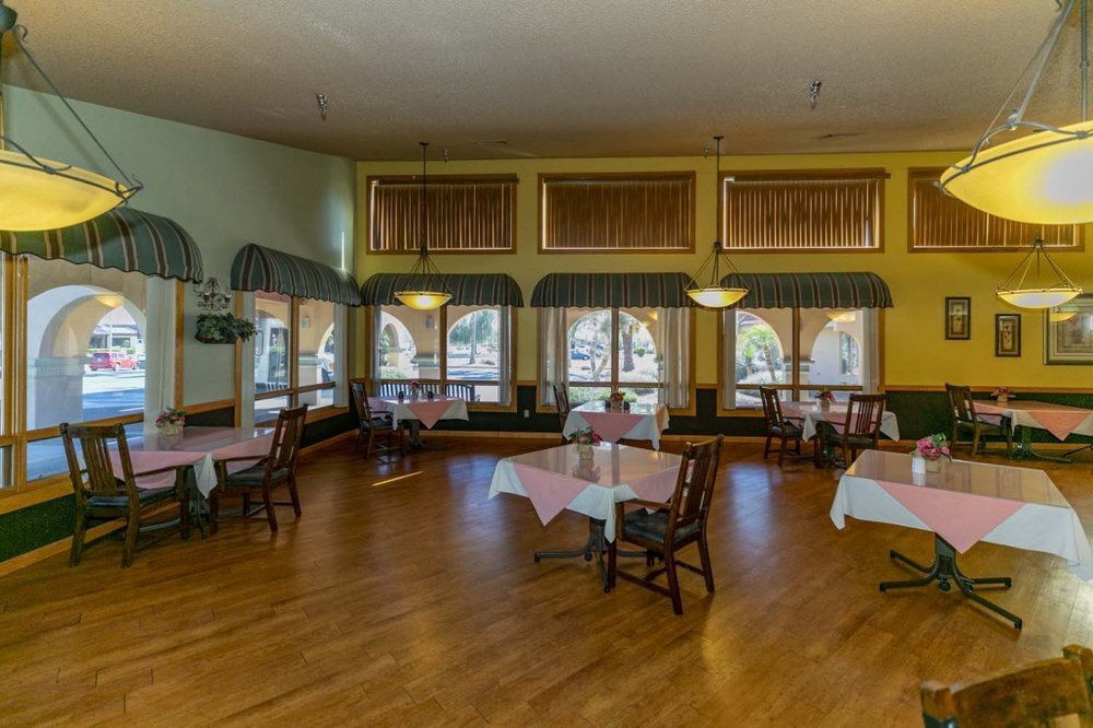 An empty restaurant dining room with neatly arranged tables and chairs on a wooden floor.