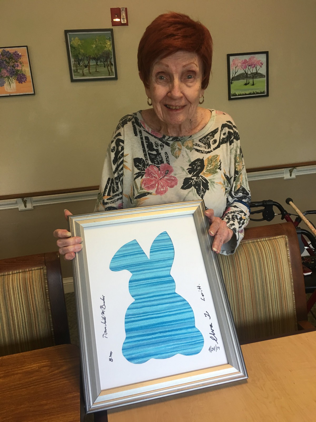 A woman holding a framed artwork of a bunny silhouette indoors.