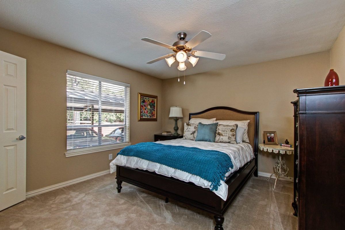 A cozy bedroom featuring a neatly made bed with a blue throw, flanked by bedside tables and illuminated by a ceiling fan light.
