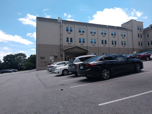 A view of a parking lot in front of a building, with several cars parked and a partly cloudy sky.