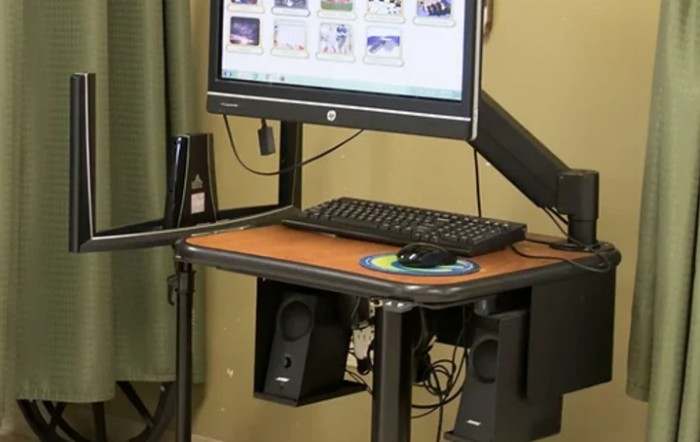 A standing desk setup with a computer monitor, keyboard, mouse, and speakers.