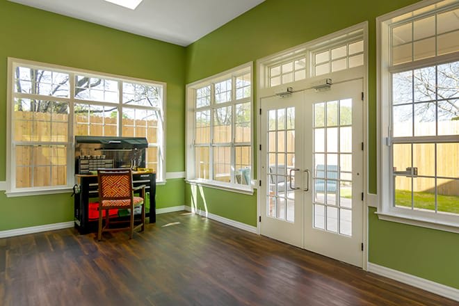 A bright room with green walls featuring large windows, a piano, and French doors.