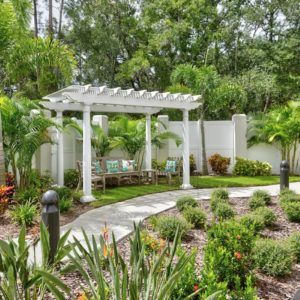 A serene garden featuring a white pergola surrounded by lush greenery and a winding pathway.