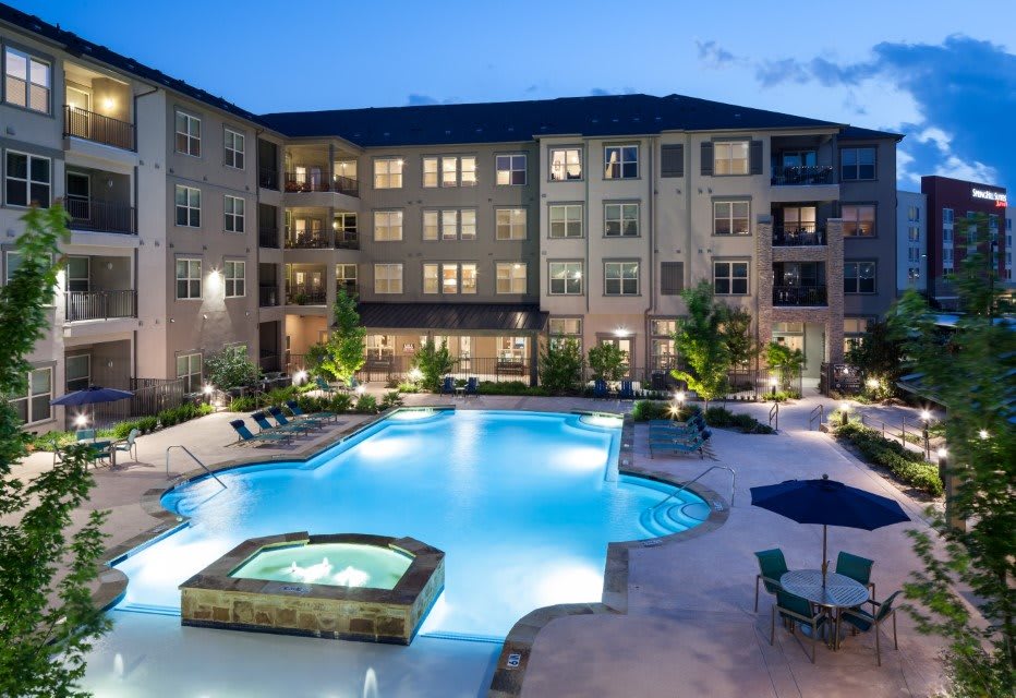 A luxurious apartment complex with a central swimming pool illuminated at night.