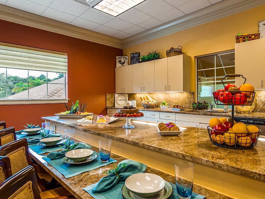 A beautifully arranged kitchen with a granite countertop and dining area set for a meal, featuring fruit displays and elegant place settings.