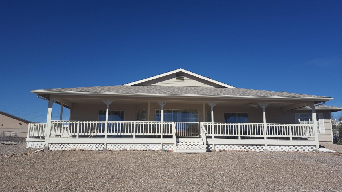 A single-story house with a large front porch under a clear blue sky.