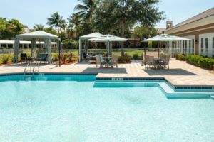 A tranquil outdoor pool area with umbrellas and seating, surrounded by palm trees.
