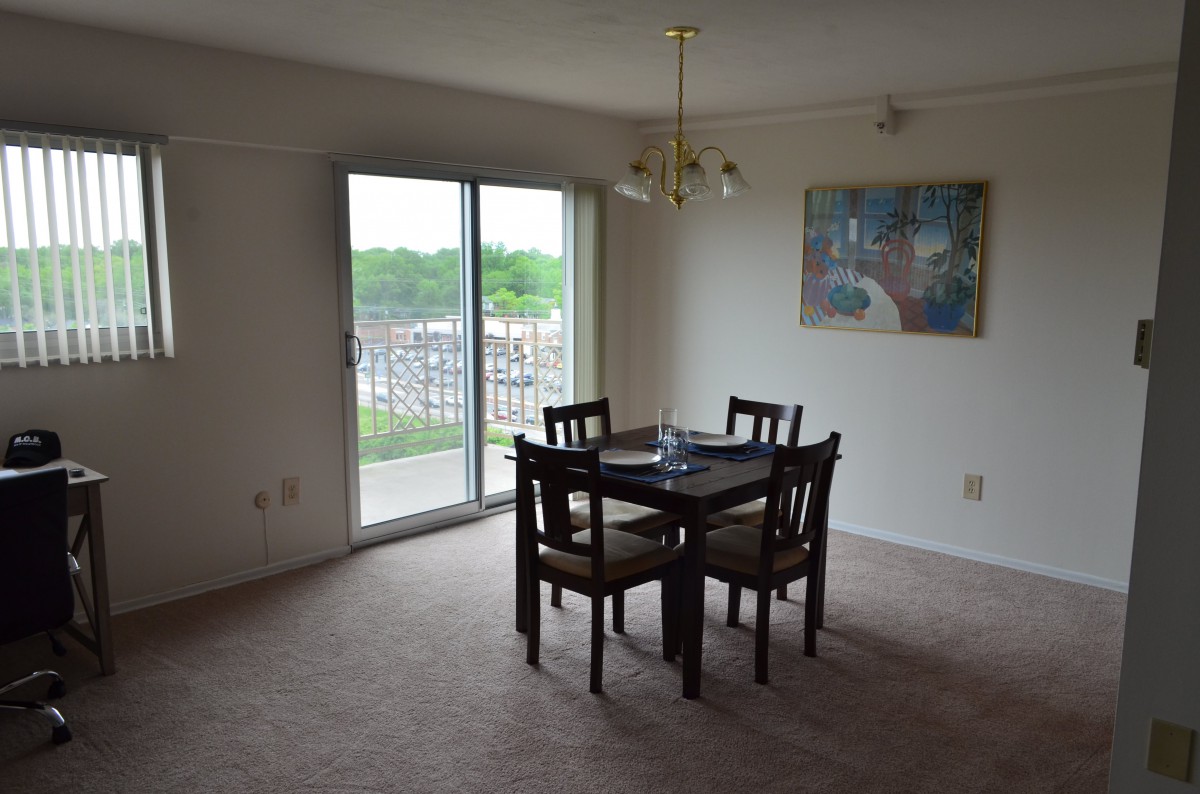 A dining area with a table and four chairs, featuring a sliding glass door leading to a balcony and wall art for decoration.