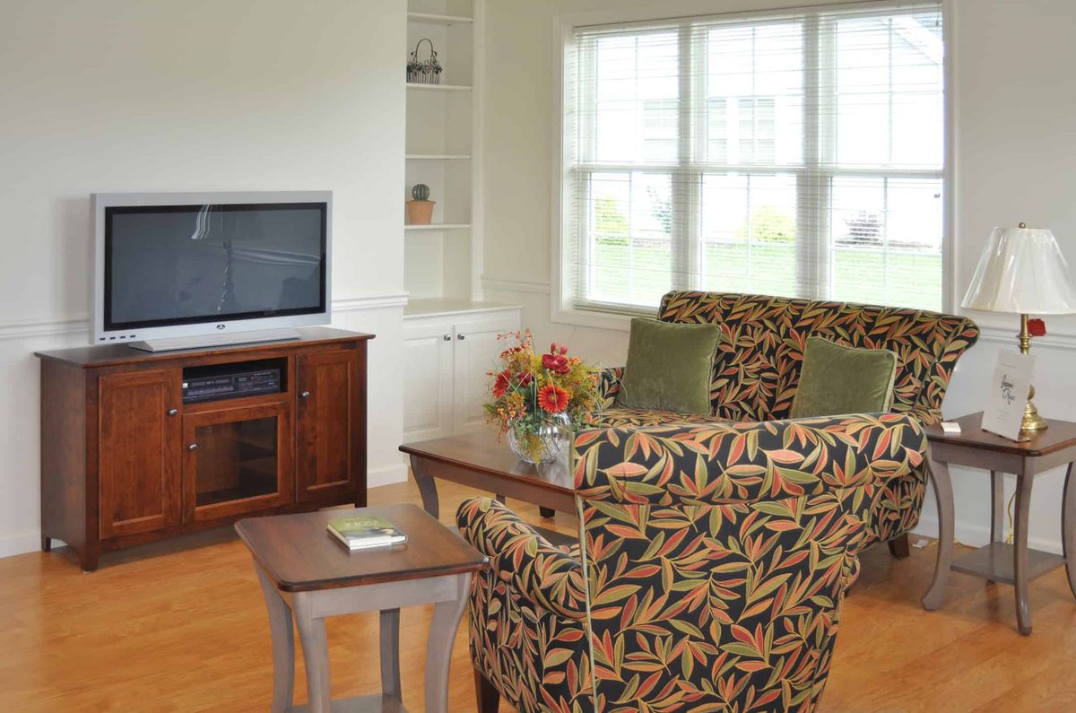 A cozy living room with patterned armchairs, a wooden entertainment center, and large windows.