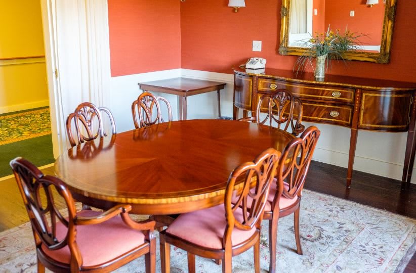 A traditionally styled dining room with a wooden oval table and matching chairs, set against warm-colored walls.