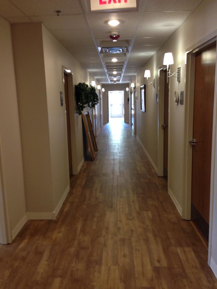 A long, well-lit hallway with wooden flooring and doors on either side.
