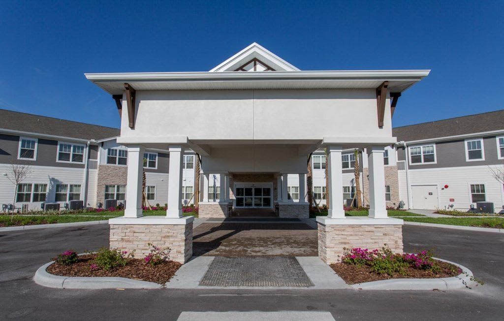 A modern residential building with a covered entrance and columns against a clear blue sky.