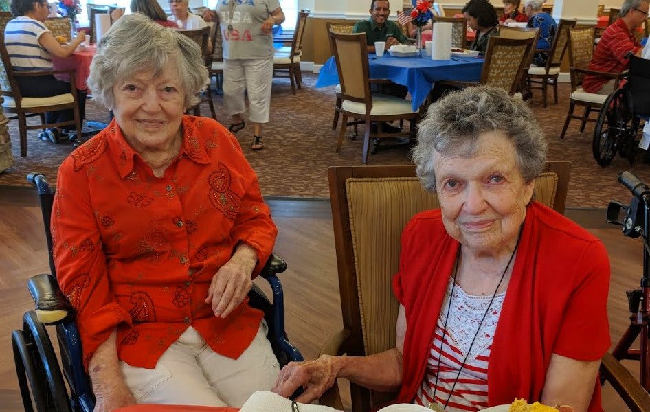 Two elderly women sitting at a table during a social gathering.